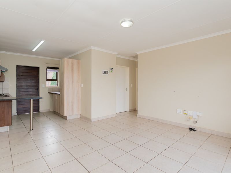 Open plan living area featuring tiled flooring, a compact kitchen with built-in cabinetry, and direct access to an exterior door.