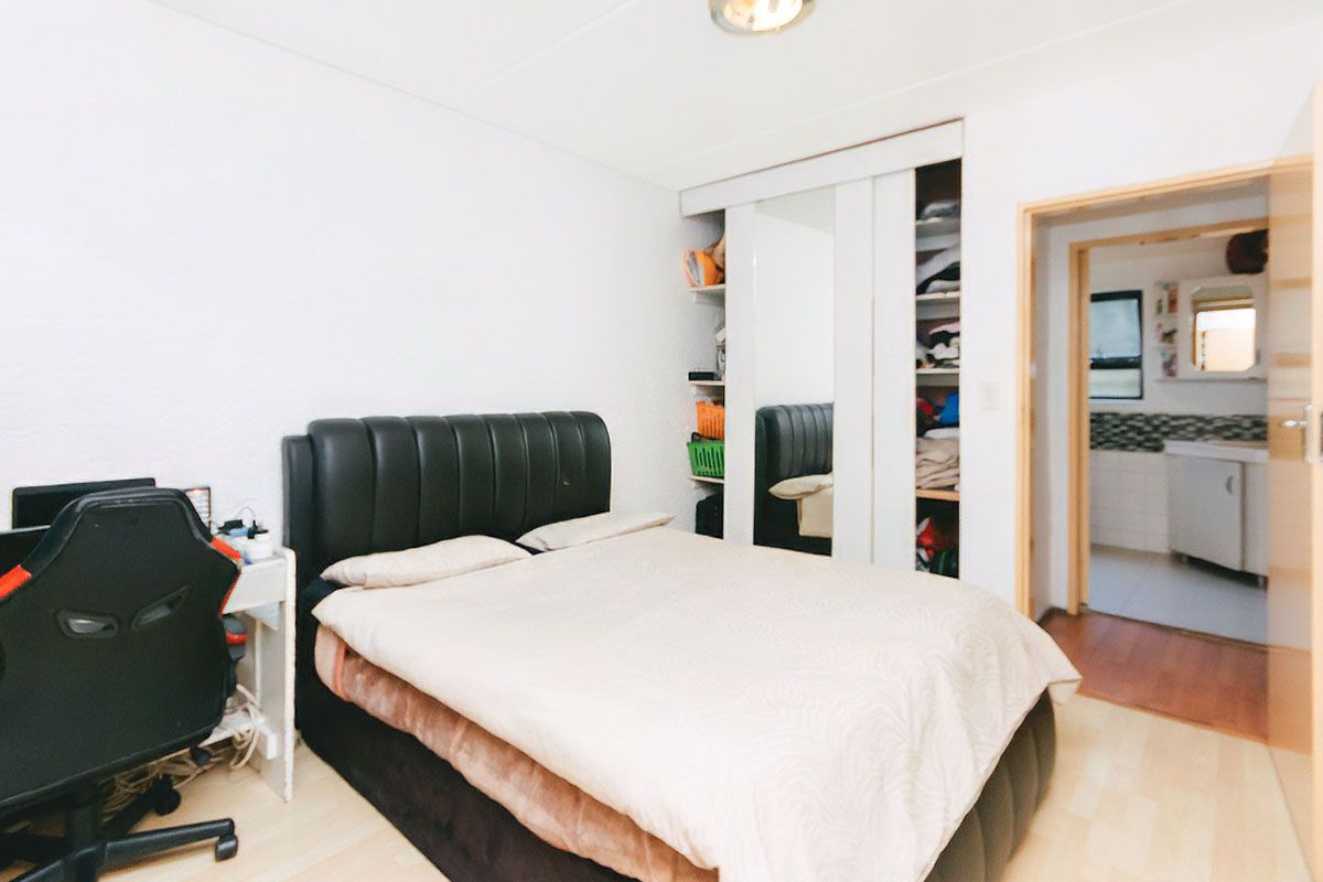 A bedroom featuring built-in sliding door cupboards with mirrored panels and laminate flooring, with an adjacent view into a tiled bathroom area.