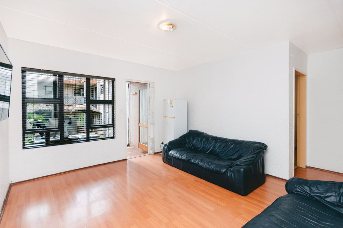 A living room featuring laminate wood flooring, large windows with black frames, and direct access to an outdoor patio area.