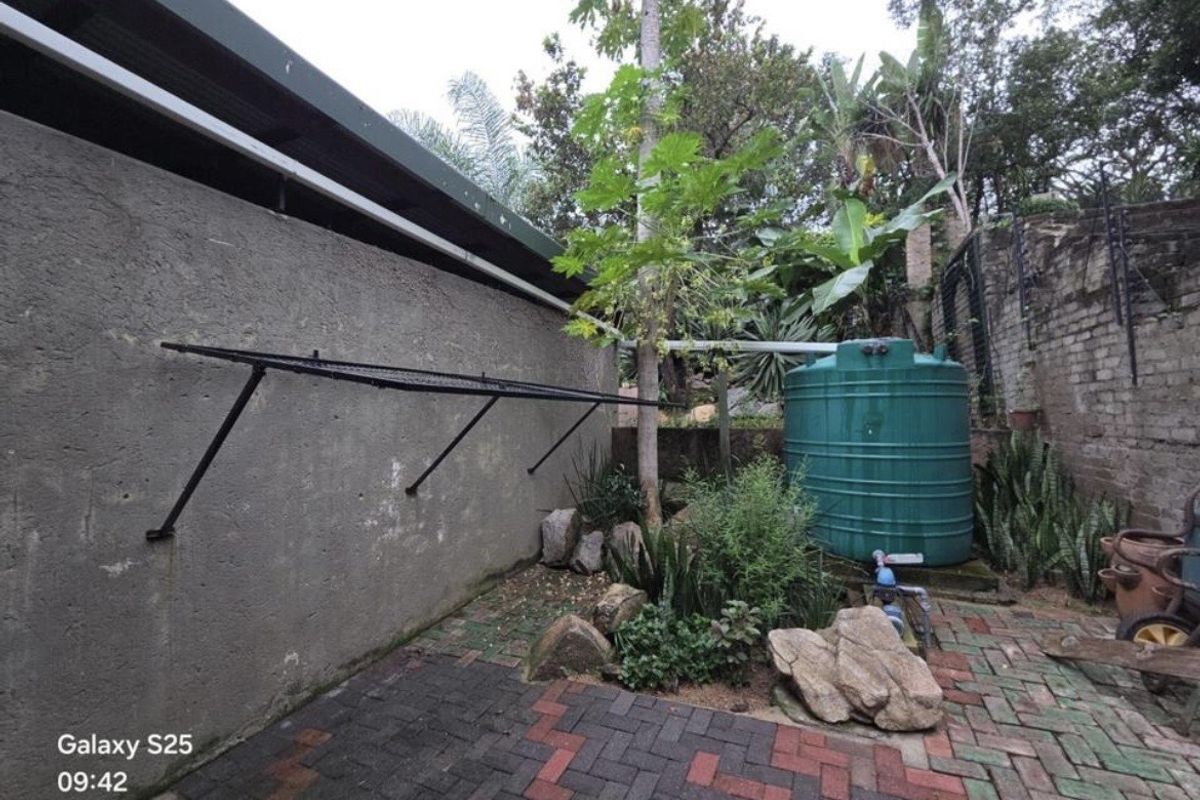 A functional rear exterior area featuring a paved courtyard, a large water storage tank, and a wall-mounted drying rack.