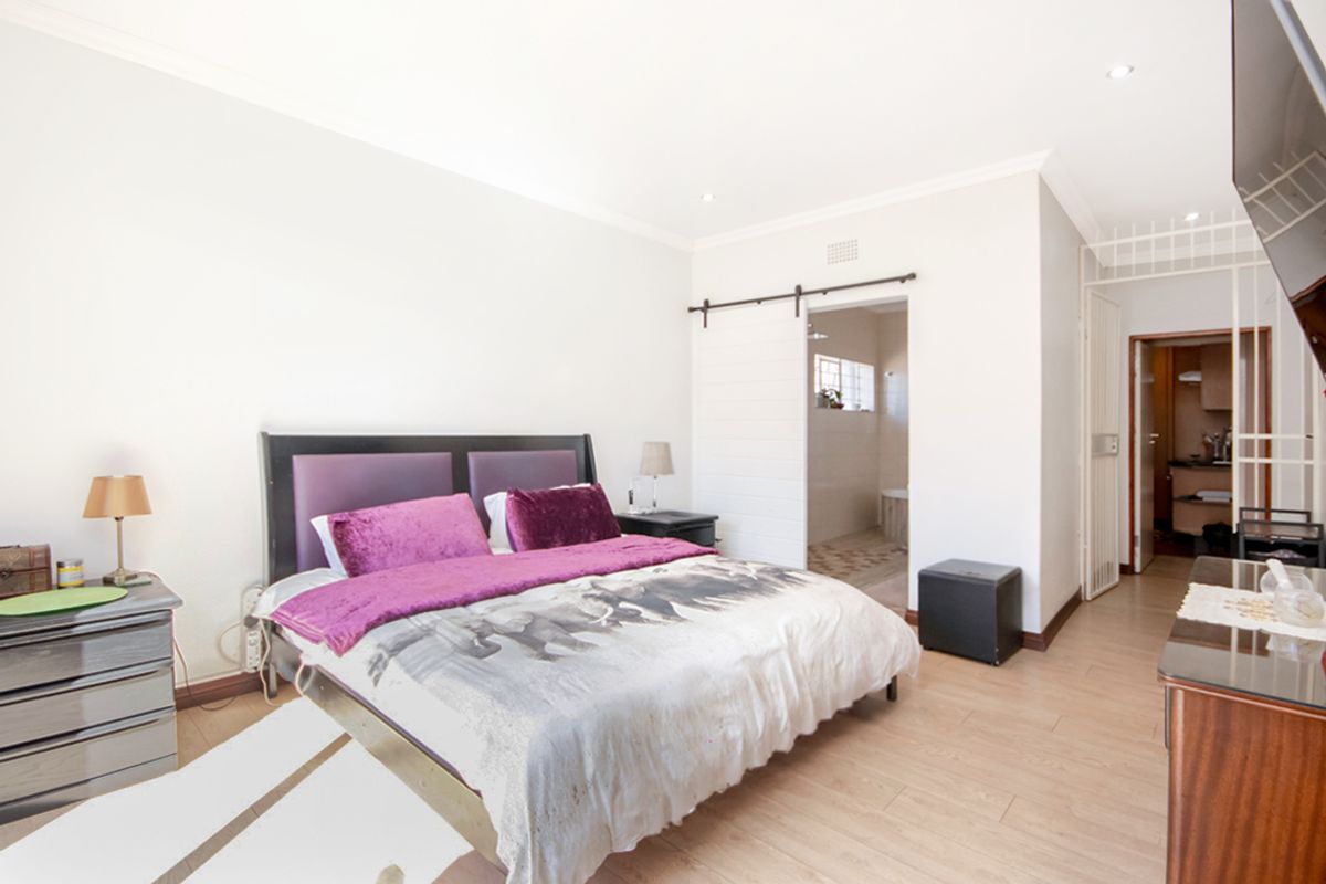 A well-lit bedroom featuring light wood-look flooring, recessed ceiling lighting, and a sliding barn-style door leading to an en-suite bathroom.