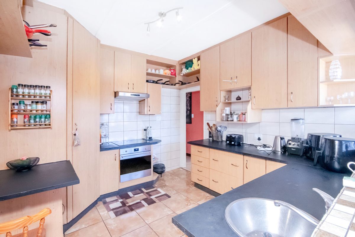 A functional kitchen featuring light wood cabinetry, dark laminate countertops, tiled splashbacks, and a built-in oven with an extractor fan.