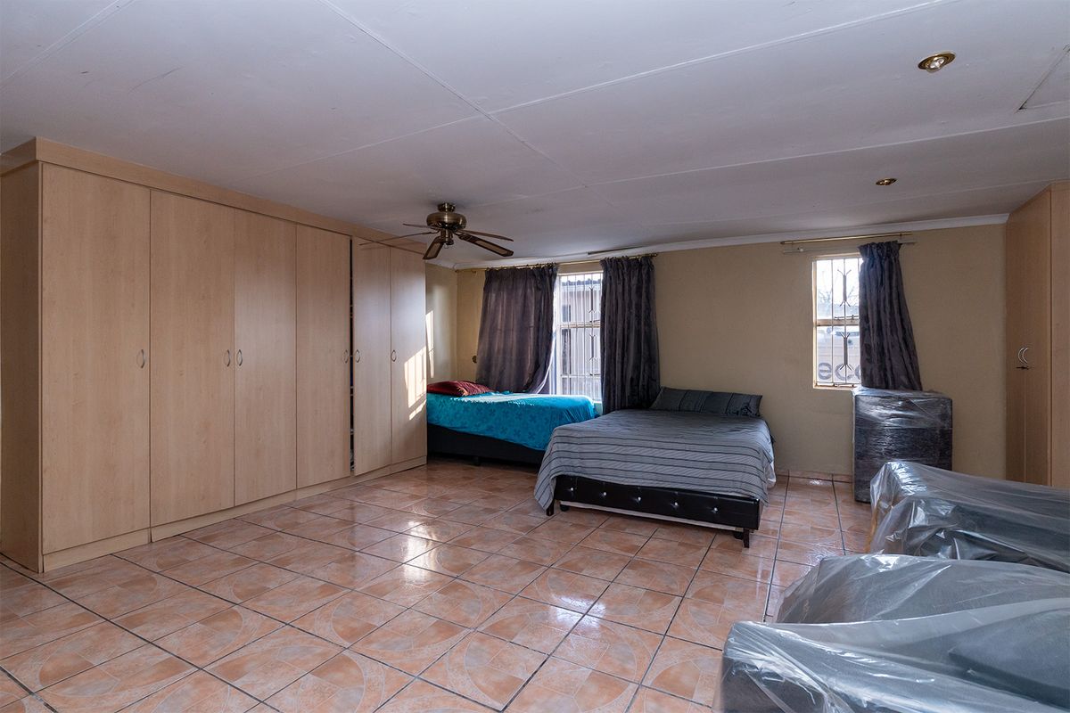 Spacious bedroom featuring extensive built-in wooden cabinetry, tiled flooring, and a ceiling fan, offering ample storage and functional living space.