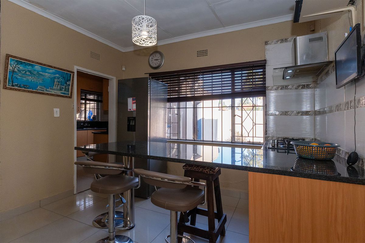 A functional kitchen featuring granite countertops, a breakfast bar, built-in cabinetry, and a stainless steel extractor fan, with an adjacent scullery area.