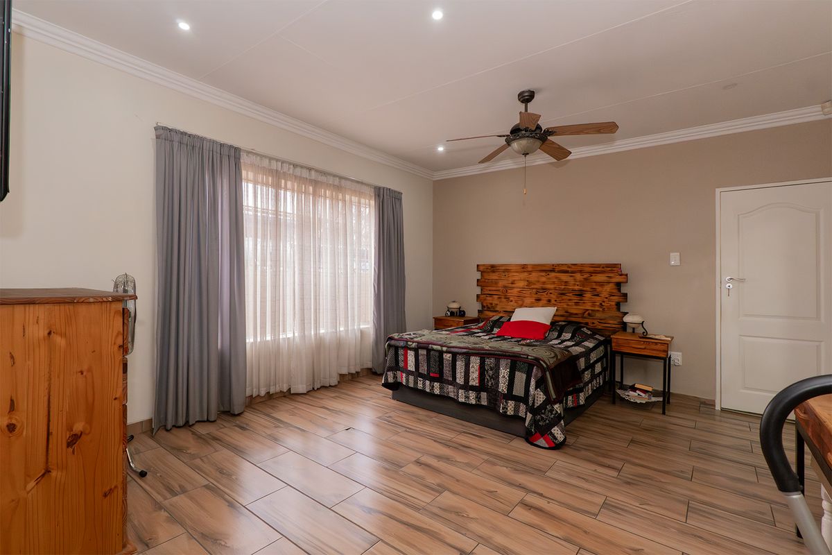 Spacious bedroom featuring wood-look tile flooring, recessed lighting, a ceiling fan, and neutral wall tones with classic cornice detailing.