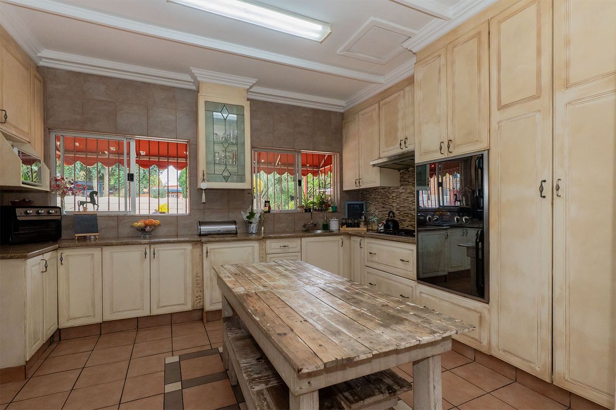 A spacious kitchen featuring traditional cream cabinetry, tiled flooring, a tiled backsplash, and integrated appliances, offering a functional layout with ample storage space.