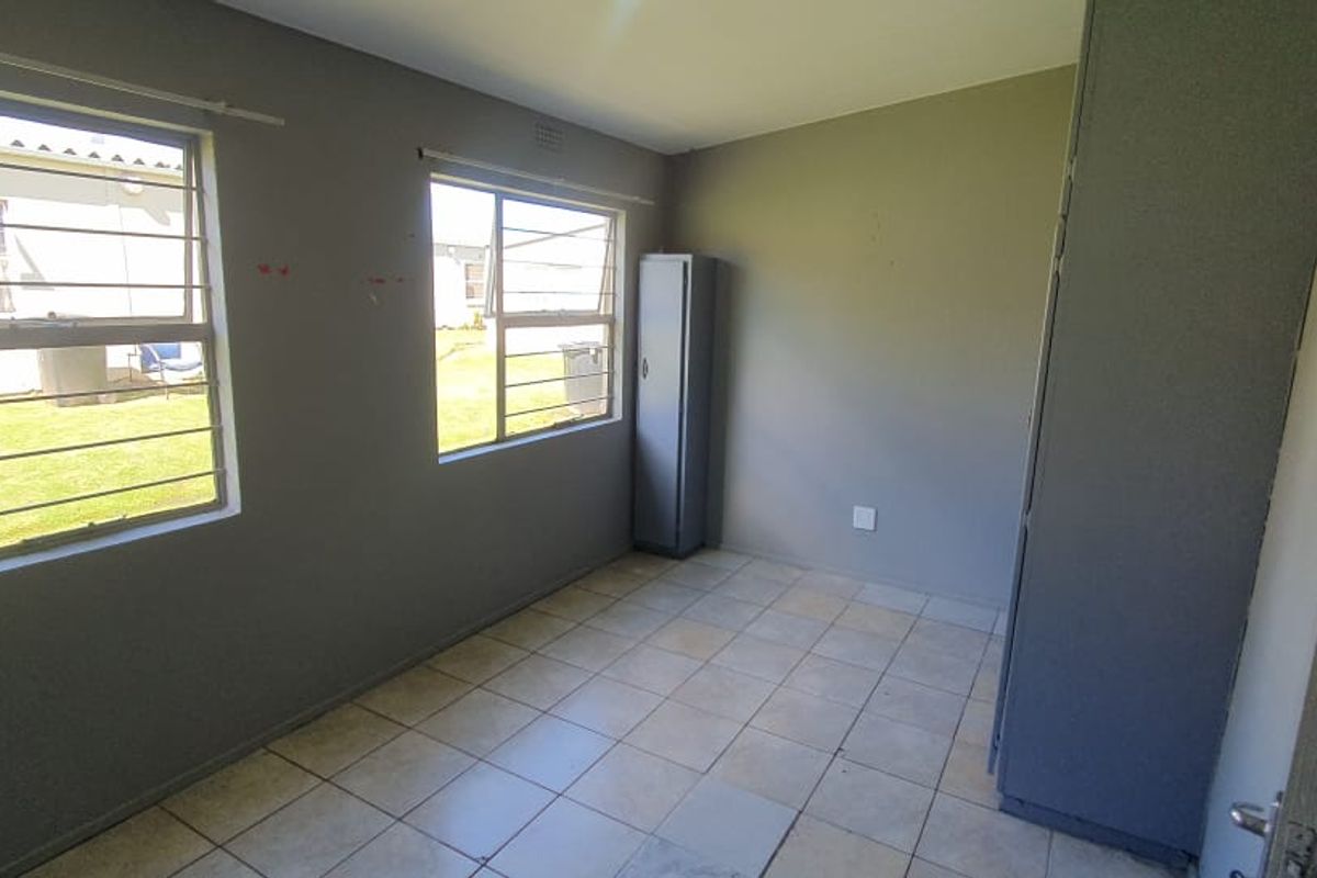 A bedroom featuring tiled flooring, built-in cupboards, and large windows with security bars, offering a functional and well-lit living space.