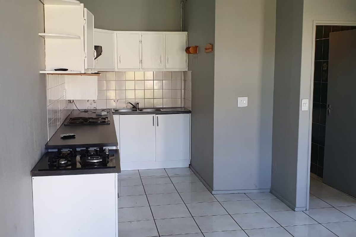 A functional kitchen featuring white cabinetry, a built-in gas hob, double sink, and tiled flooring, adjacent to a doorway leading to another room.