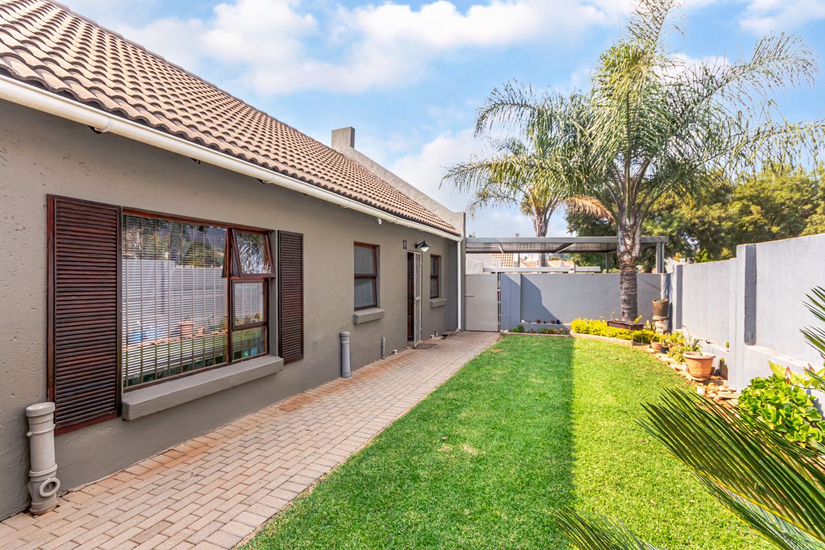 A well-maintained rear exterior view of the townhouse featuring a paved walkway, manicured lawn, boundary walls, and secure gated access.