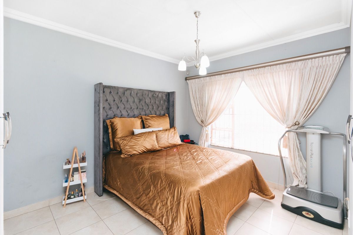 A well-maintained bedroom featuring tiled flooring, crown molding, and a central light fixture, offering a clean and functional living space.
