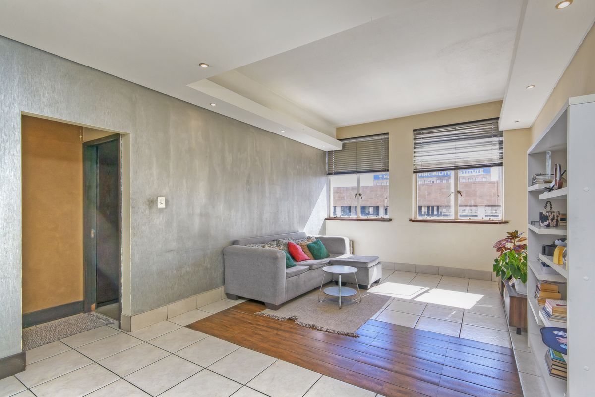 A living room featuring a mix of tiled and laminate flooring, a textured feature wall, recessed ceiling lighting, and large windows with venetian blinds.