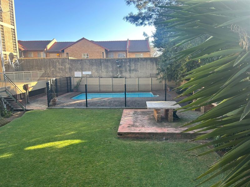 A private outdoor area featuring a swimming pool, paved patio space, built-in brick table, and a well-maintained lawn within a secure complex setting.