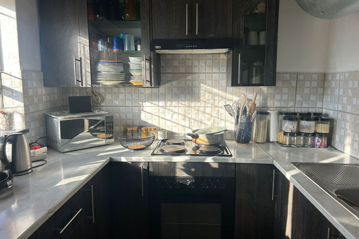 A compact kitchen featuring dark wood cabinetry, a built-in oven with a hob, an extractor fan, and tiled splashbacks with light-colored countertops.