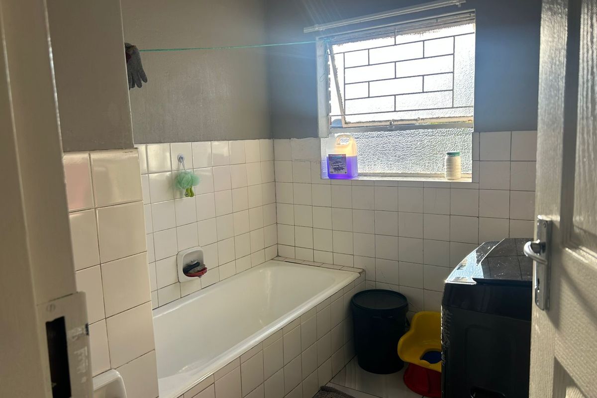 A functional bathroom featuring a built-in bathtub with white wall tiling and a window providing natural light.