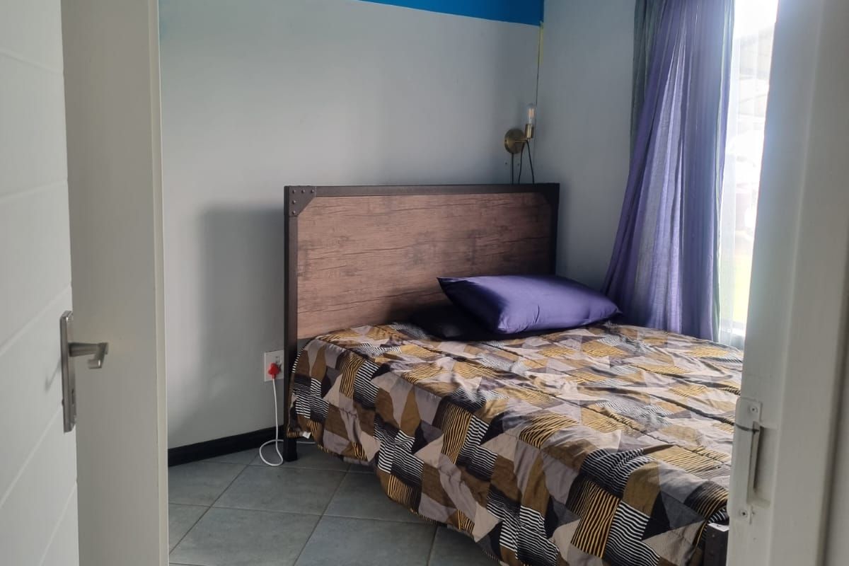 A compact bedroom featuring tiled flooring, a blue painted ceiling, and a window with curtain fixtures.
