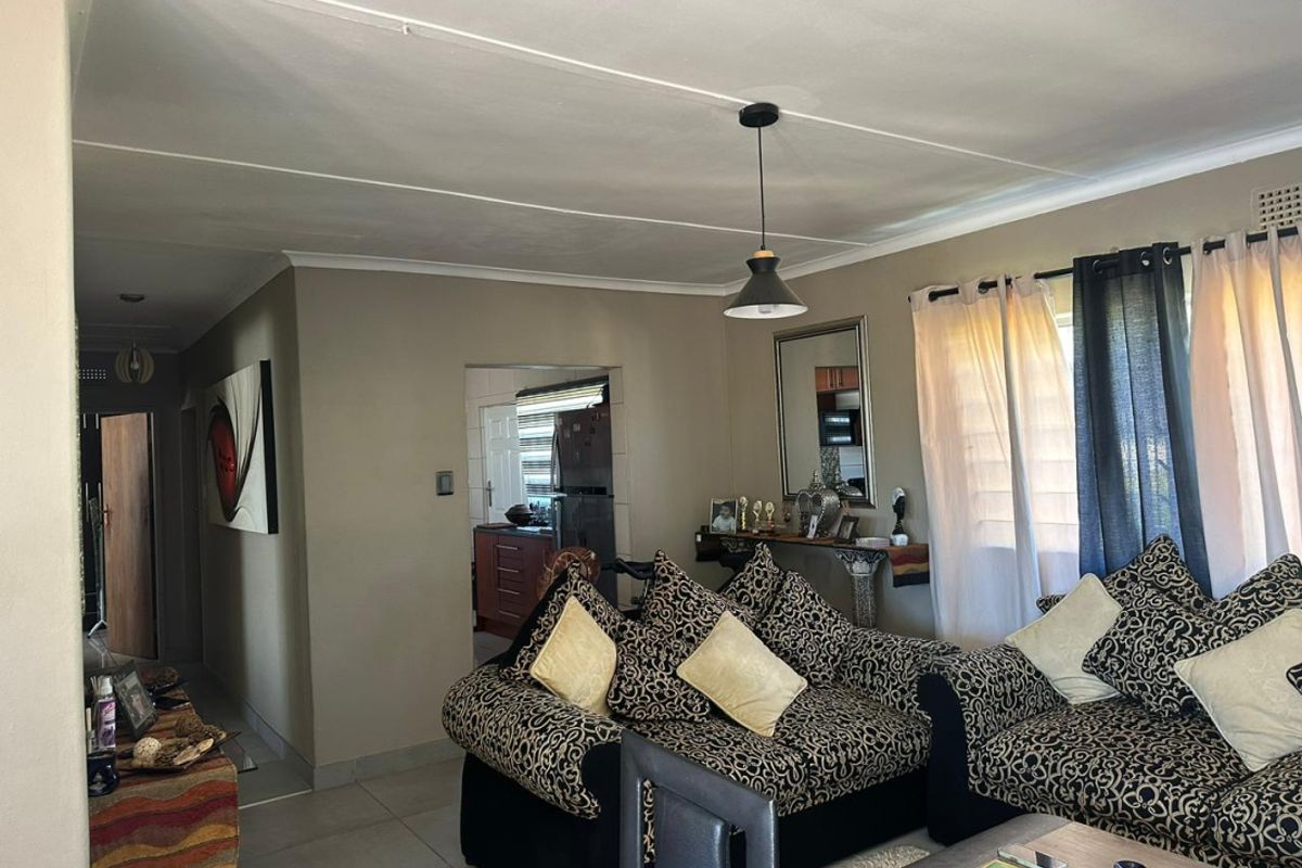 A comfortable living room featuring tiled flooring, neutral wall tones, and a pendant light fixture, with an open transition to the kitchen area.