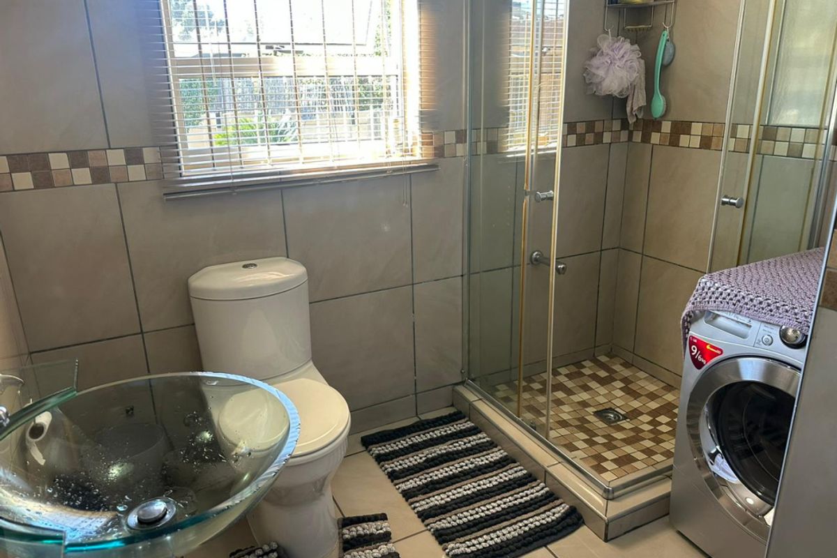 A functional bathroom featuring a glass vessel sink, a walk-in shower with glass enclosure, and a built-in space for a washing machine.