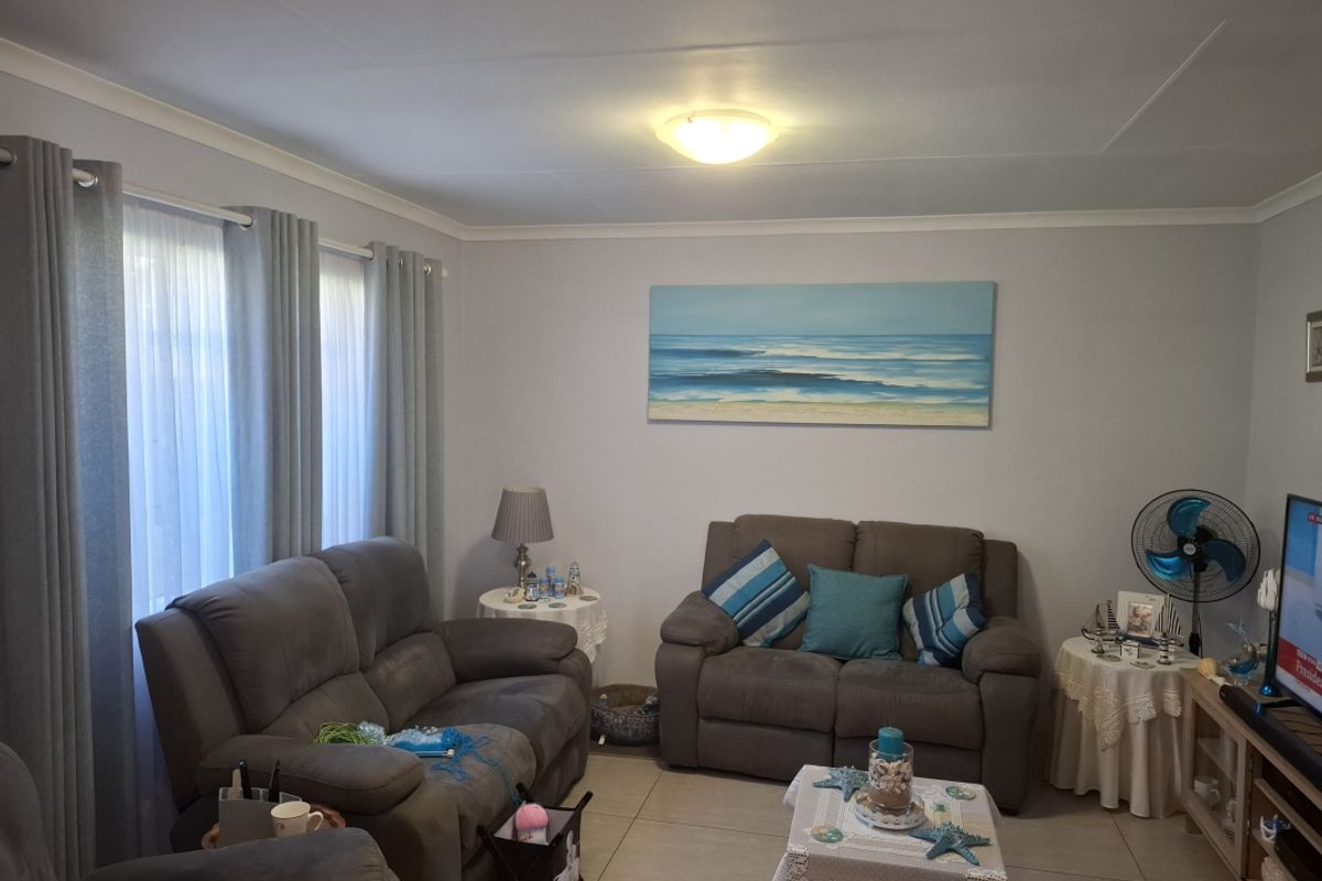 A comfortable living room featuring neutral tiled flooring, coved ceiling cornices, and large windows with fitted curtain tracks.
