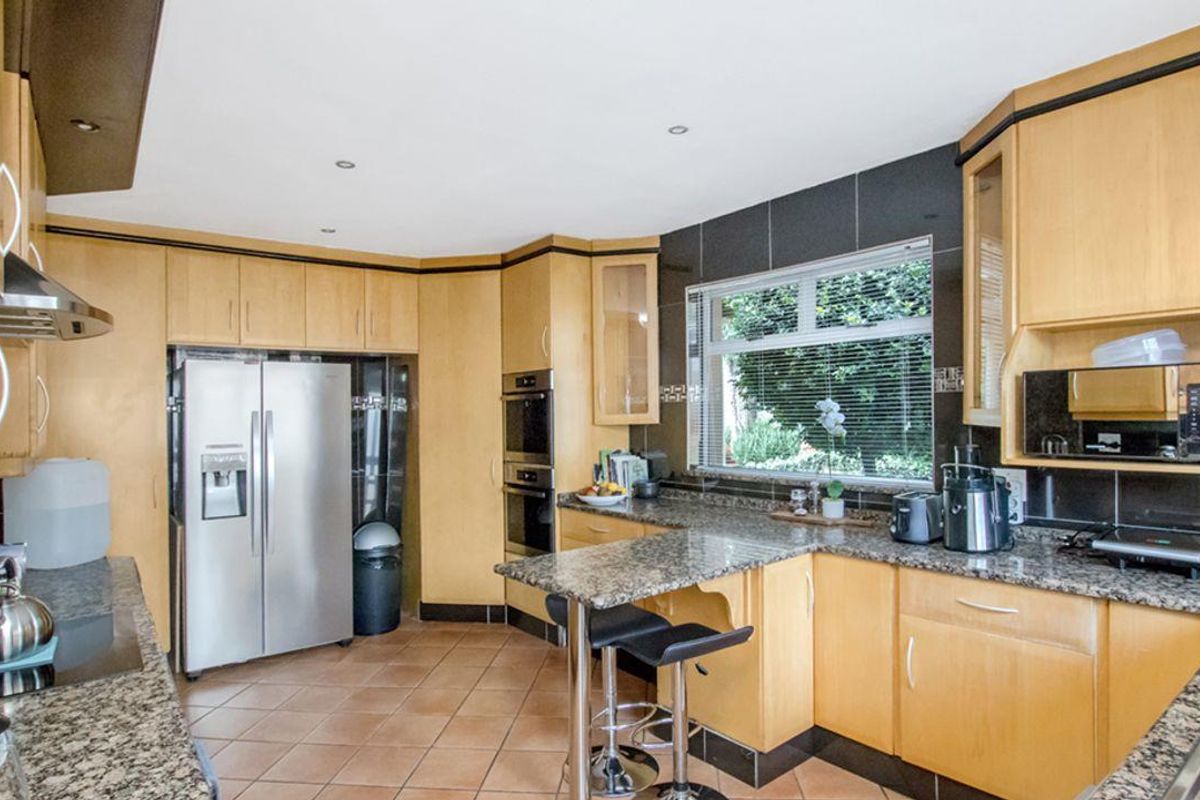 A functional kitchen featuring light wood cabinetry, granite countertops, integrated oven, and a breakfast bar area with tiled flooring.