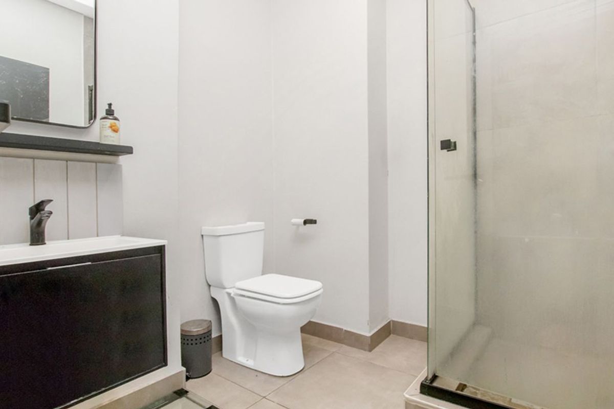 A modern bathroom featuring a glass-enclosed shower, a sleek vanity with a basin, and a standard toilet with neutral floor tiling.