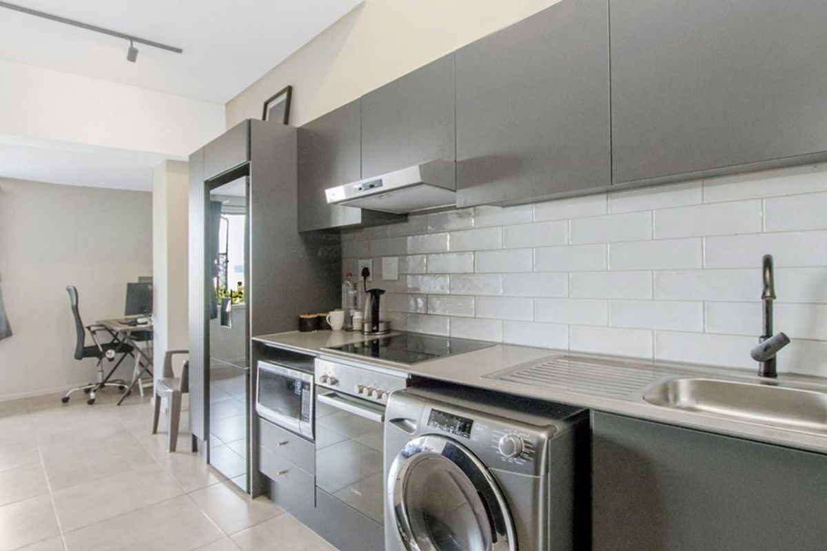 Modern kitchen featuring sleek grey cabinetry, subway tile backsplash, integrated oven, hob, extractor fan, and a stainless steel sink with a contemporary faucet.
