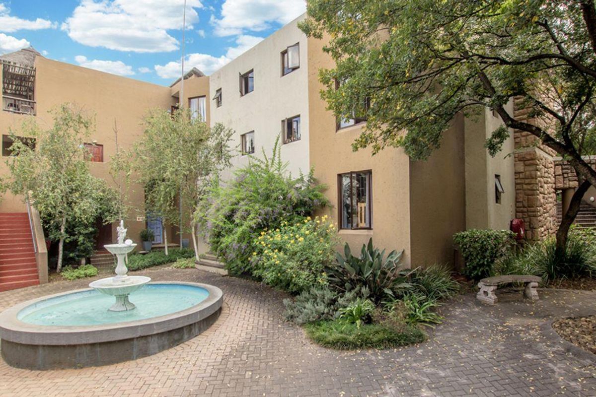 A view of the townhouse complex courtyard featuring a central water fountain, paved walkways, and established landscaping surrounding the multi-story residential building.