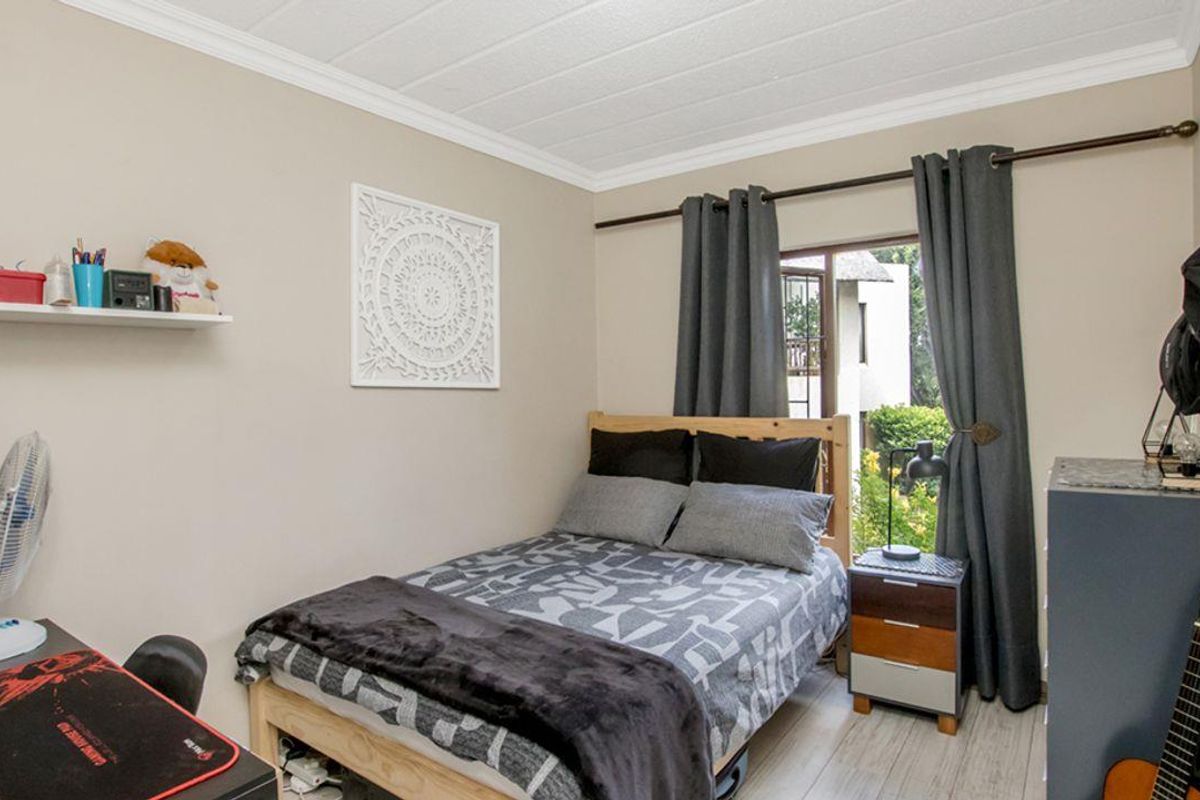 A functional bedroom featuring light-toned flooring, crown molding, and a window with garden views, providing a comfortable and well-lit living space.