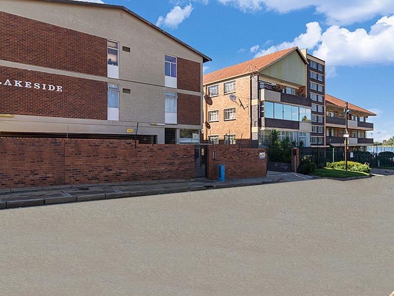 Exterior view of the Lakeside apartment complex, featuring a brick boundary wall, electric fencing, and multi-story residential units.