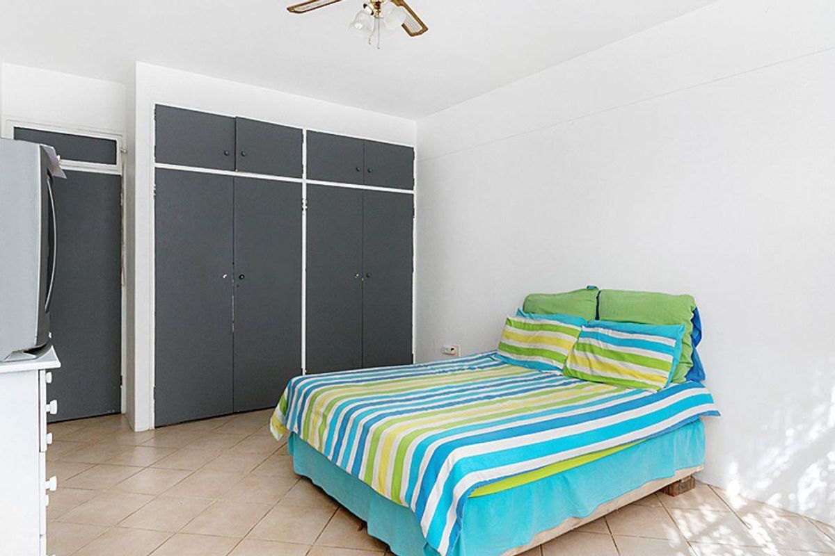 A functional bedroom featuring tiled flooring, a ceiling fan, and ample built-in cupboard storage space.