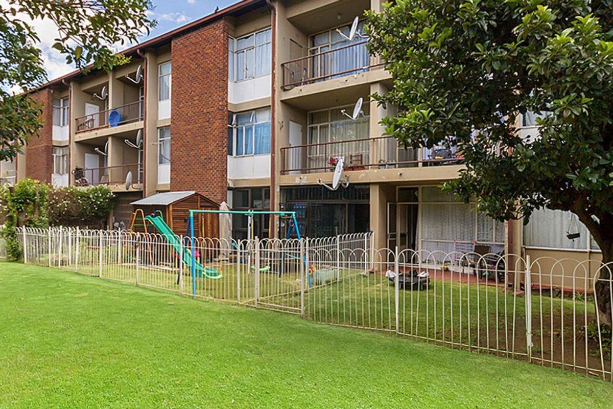 Rear view of a multi-story apartment building featuring brick facade, private balconies with metal railings, and access to a shared communal garden area.