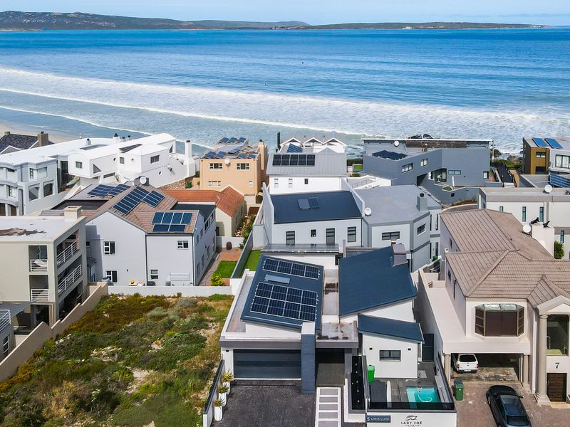 Aerial view of a coastal residential property featuring solar panels, a private swimming pool, and direct proximity to the ocean.