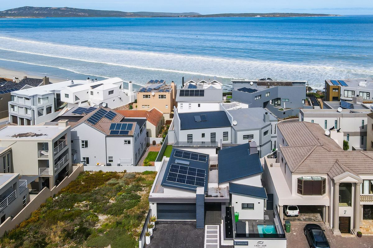 Aerial view of a coastal residential property featuring solar panels, a private swimming pool, and direct proximity to the ocean.