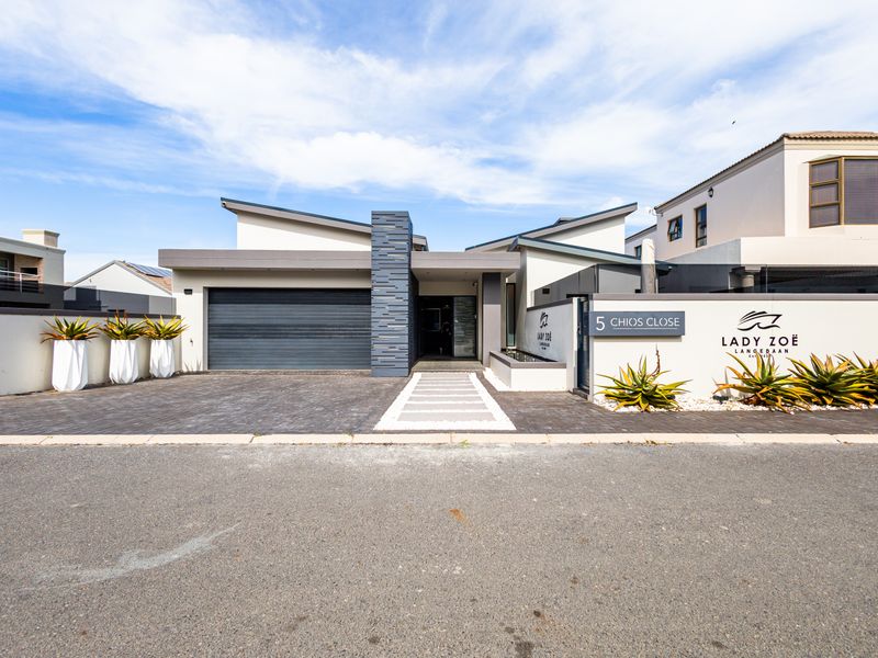 Modern front elevation of a contemporary house featuring a double garage, stone-clad architectural detail, and a paved driveway with a clean, well-maintained boundary wall.