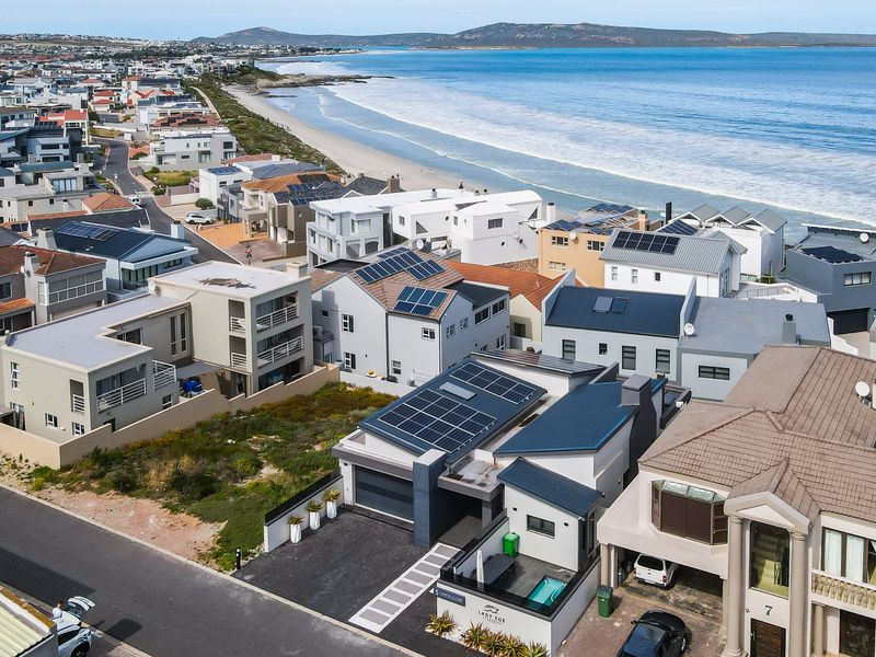 Aerial view of a coastal residential property featuring solar panels, a private swimming pool, and a paved driveway, situated near the beach.