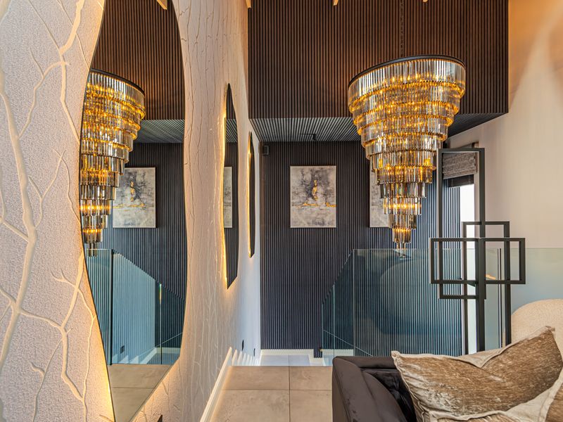 A sophisticated hallway featuring modern slatted timber wall paneling, a glass balustrade, and a striking tiered chandelier, creating a luxurious and contemporary atmosphere.
