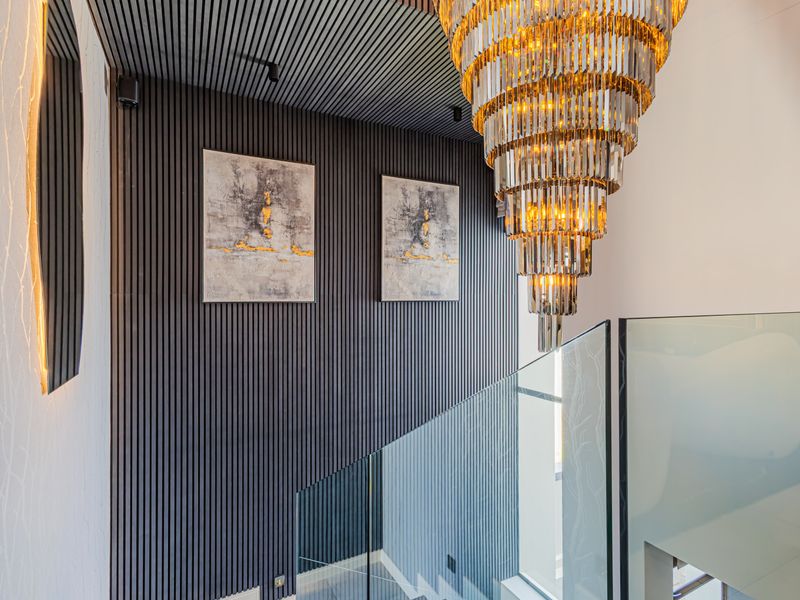 A modern, high-end staircase area featuring sophisticated slatted wall paneling, a glass balustrade, and a striking tiered crystal chandelier.