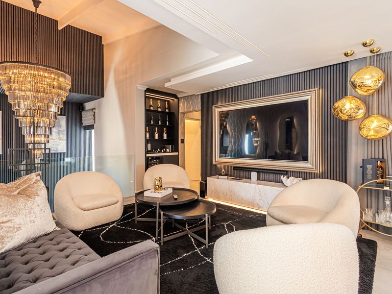 A sophisticated living room featuring dark slatted wall paneling, a marble media console, recessed ceiling lighting, and a striking crystal chandelier.