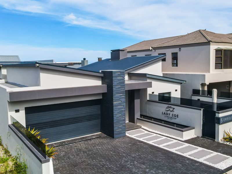 Modern front elevation featuring a paved driveway, double garage, stone-clad architectural pillar, and a sleek entrance with integrated water feature.