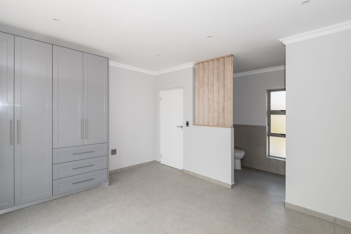 A modern bedroom featuring built-in grey cabinetry and an open-plan en-suite bathroom area with a privacy screen and tiled flooring.