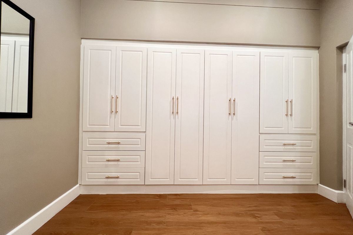 A well-maintained bedroom featuring extensive built-in cabinetry with shaker-style doors, integrated drawers, and modern hardware, complemented by wood-look flooring.