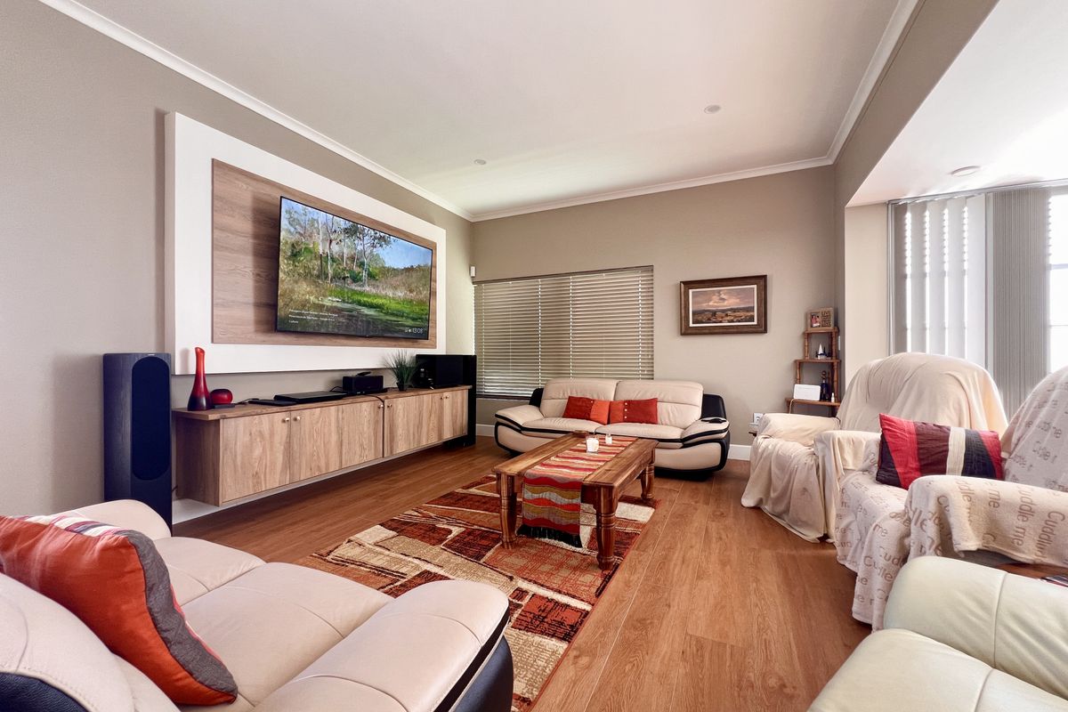 Spacious living room featuring a custom built-in media console with wood-grain cabinetry and integrated wall paneling, complemented by warm-toned laminate flooring.