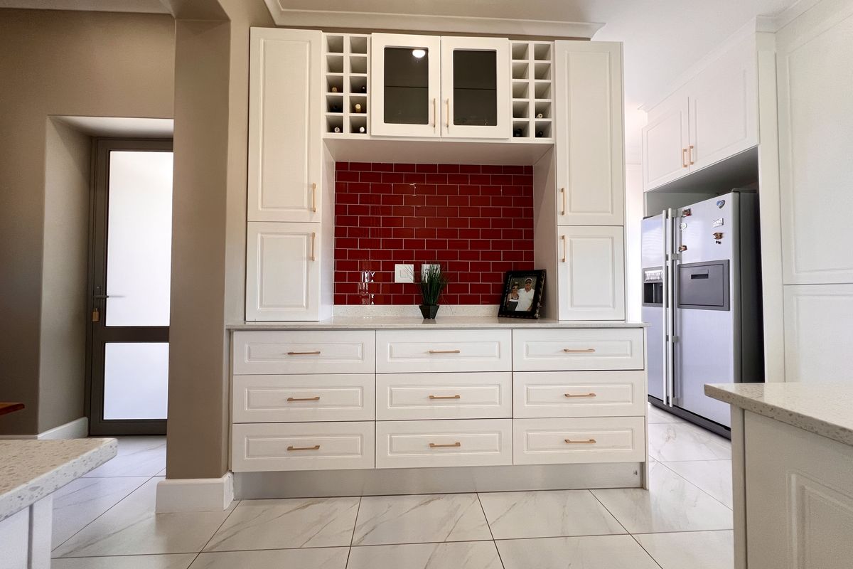 Modern kitchen featuring white shaker-style cabinetry, a striking red subway tile backsplash, and light marble-look floor tiles.