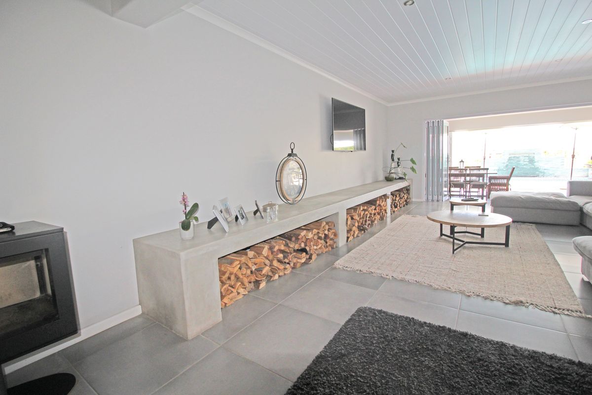 Spacious living room featuring a modern concrete built-in media console with integrated firewood storage, tiled flooring, and seamless access to the outdoor patio area.