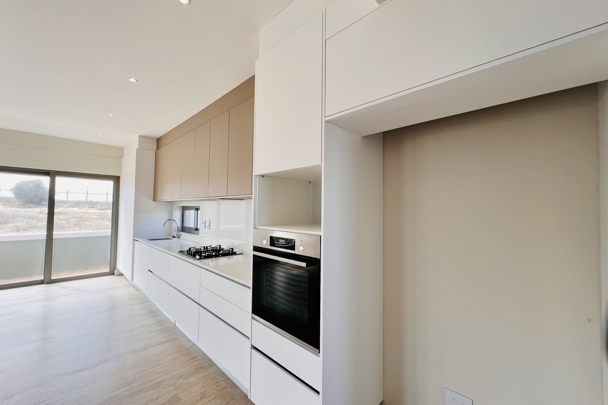 Modern kitchen featuring sleek white and beige cabinetry, built-in oven, gas hob, and integrated sink, with direct access to an outdoor balcony area.