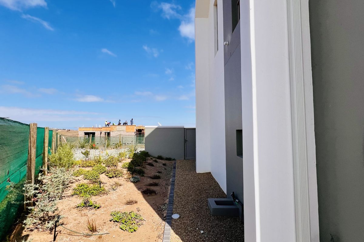 Side exterior view of the property featuring a landscaped garden bed, gravel pathway, and modern building facade with clean architectural lines.