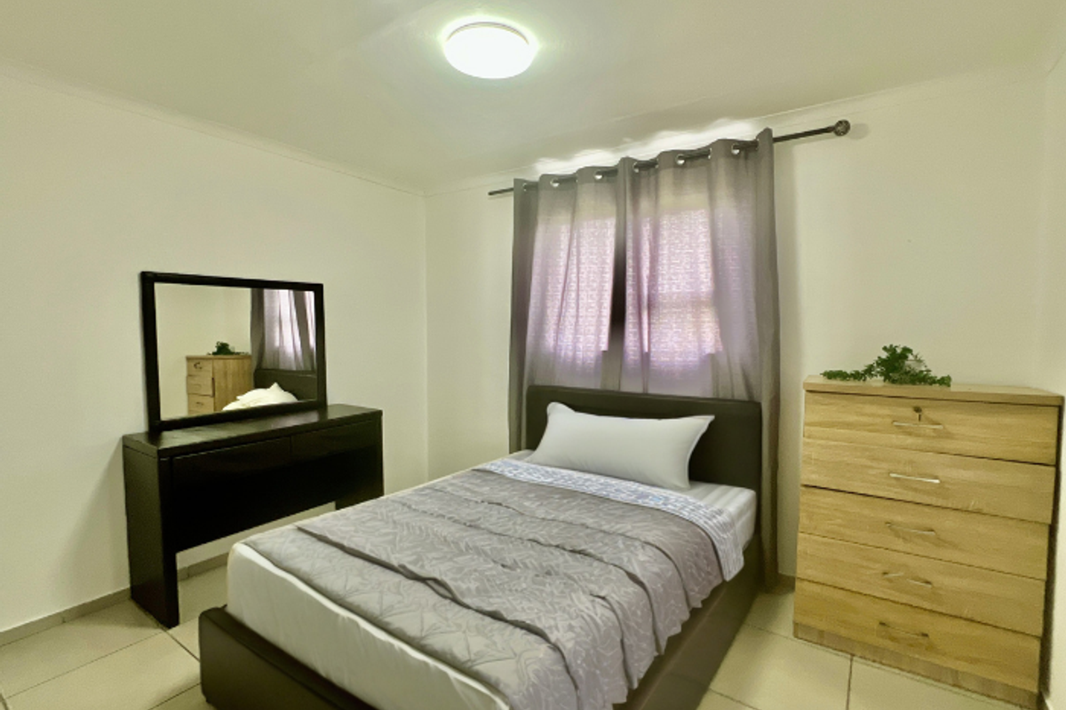 A functional bedroom featuring neutral tiled flooring, a central ceiling light fixture, and a window fitted with a curtain rod.