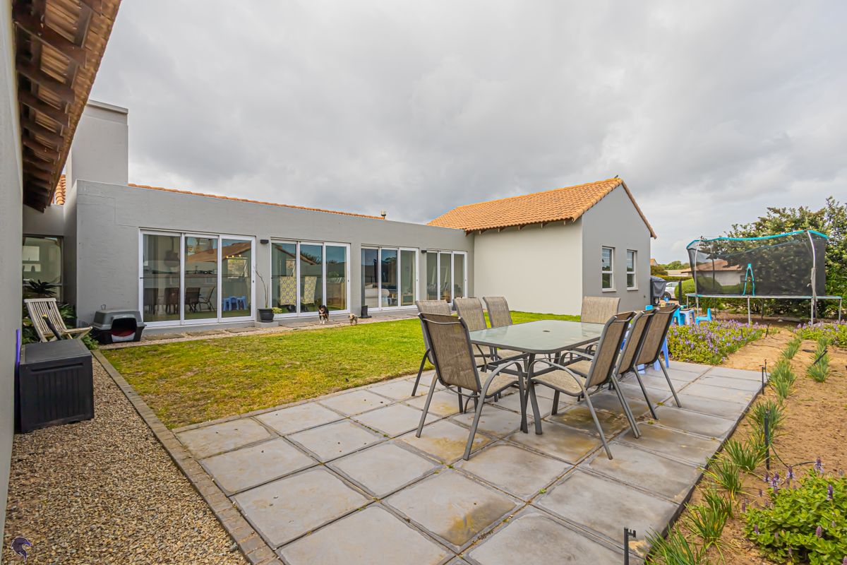 Spacious rear garden featuring a paved patio area, level lawn, and multiple sliding glass doors providing seamless indoor-outdoor flow.