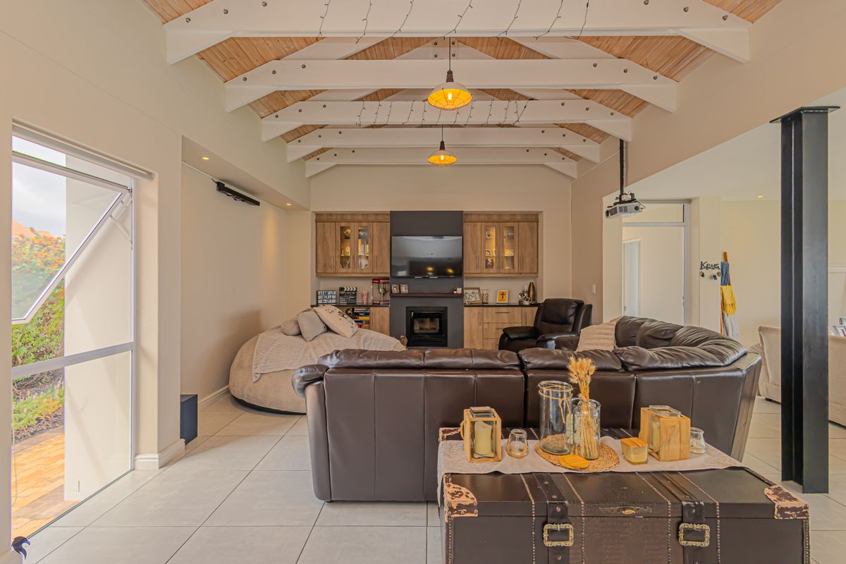 Spacious living room featuring a vaulted timber-clad ceiling with exposed beams, built-in cabinetry, a fireplace, and large windows providing natural light.