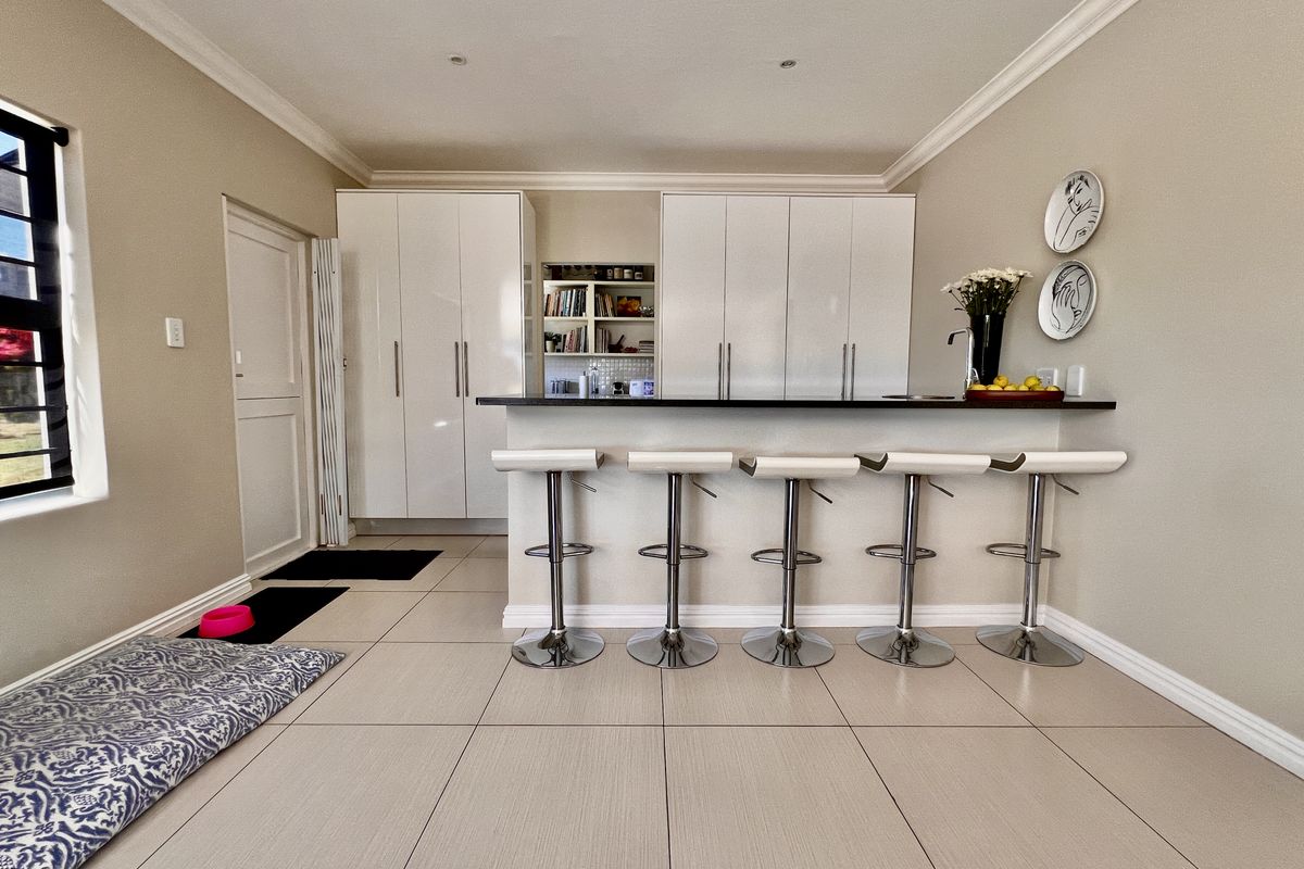 A modern kitchen area featuring sleek white cabinetry, a dark countertop breakfast bar, and large format floor tiles.