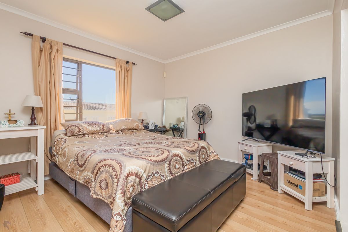 A well-lit bedroom featuring light-toned laminate flooring, neutral wall finishes, and a large window with curtain rods.